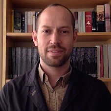 Head and shoulders photo of Nils. White male wearing a pink shirt and dark brown jacket