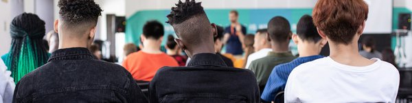 Photo of a group of young college students from behind looking at a teacher