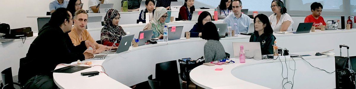 People sitting in a tiered lecture theatre listening to a person speaking at the front of the room